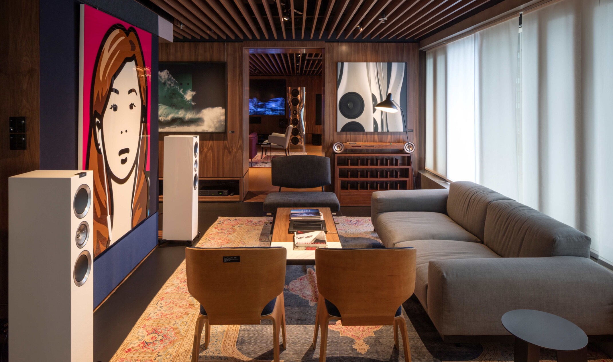 Showroom space with varied seating; couch; chairs and stools face speakers and artwork; background dark wood to another furniture showroom space