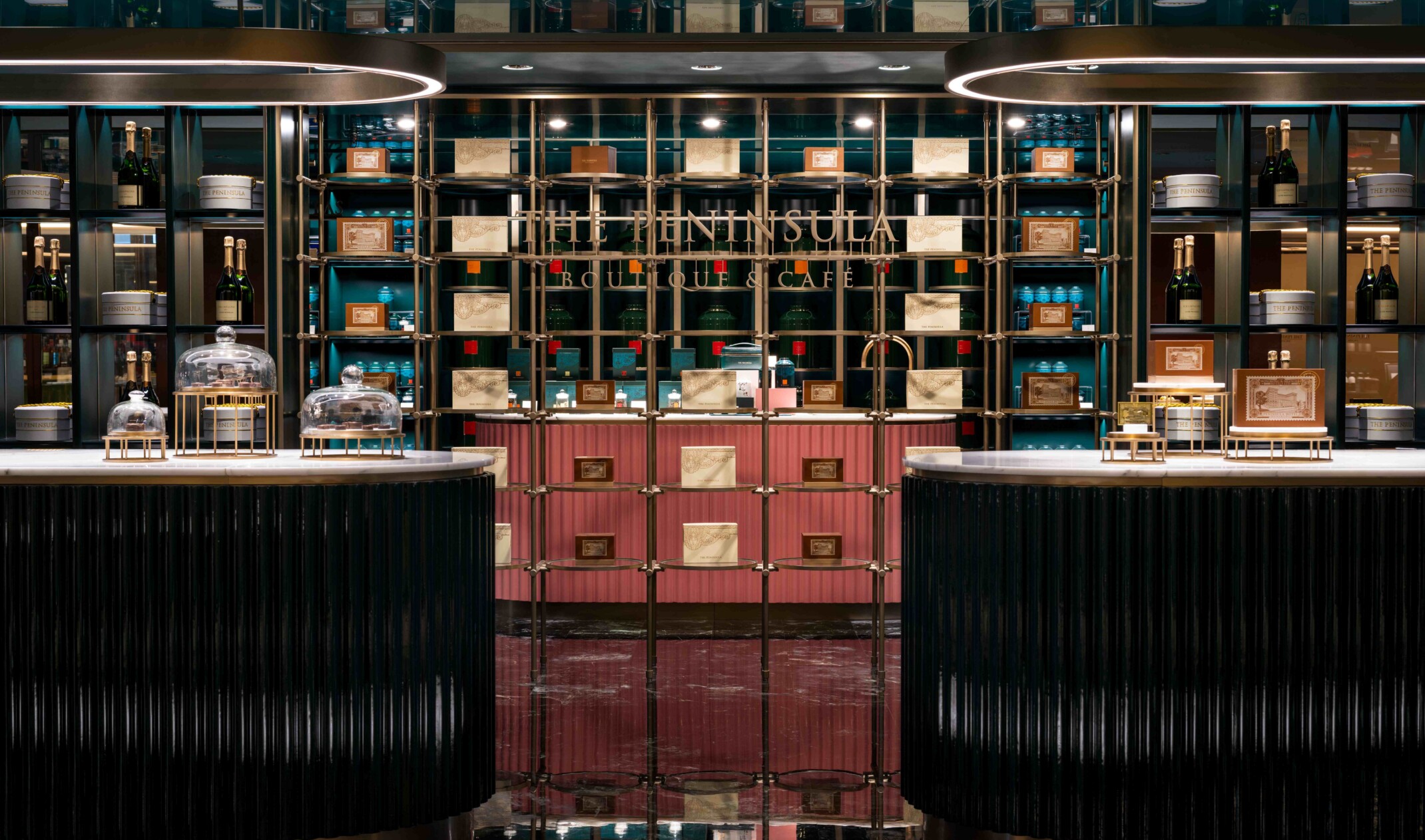 Modern, dimly lit cafe for the Peninsula Cafe; marble, sleek counters in front of a maximalist shelving showcasing wine, art, and branded item