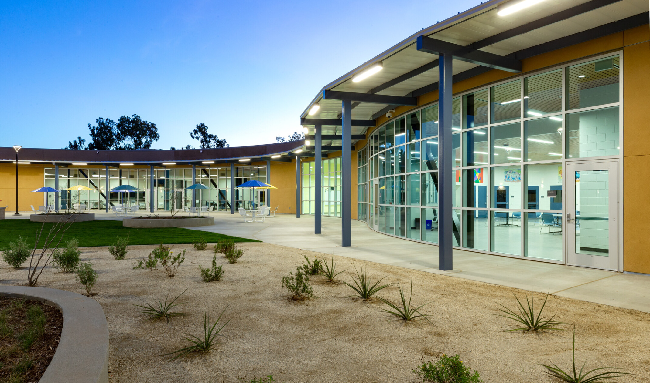 curved single story building with flat roof floor to ceiling glass facade with yellow panels. concrete paths in desertscape