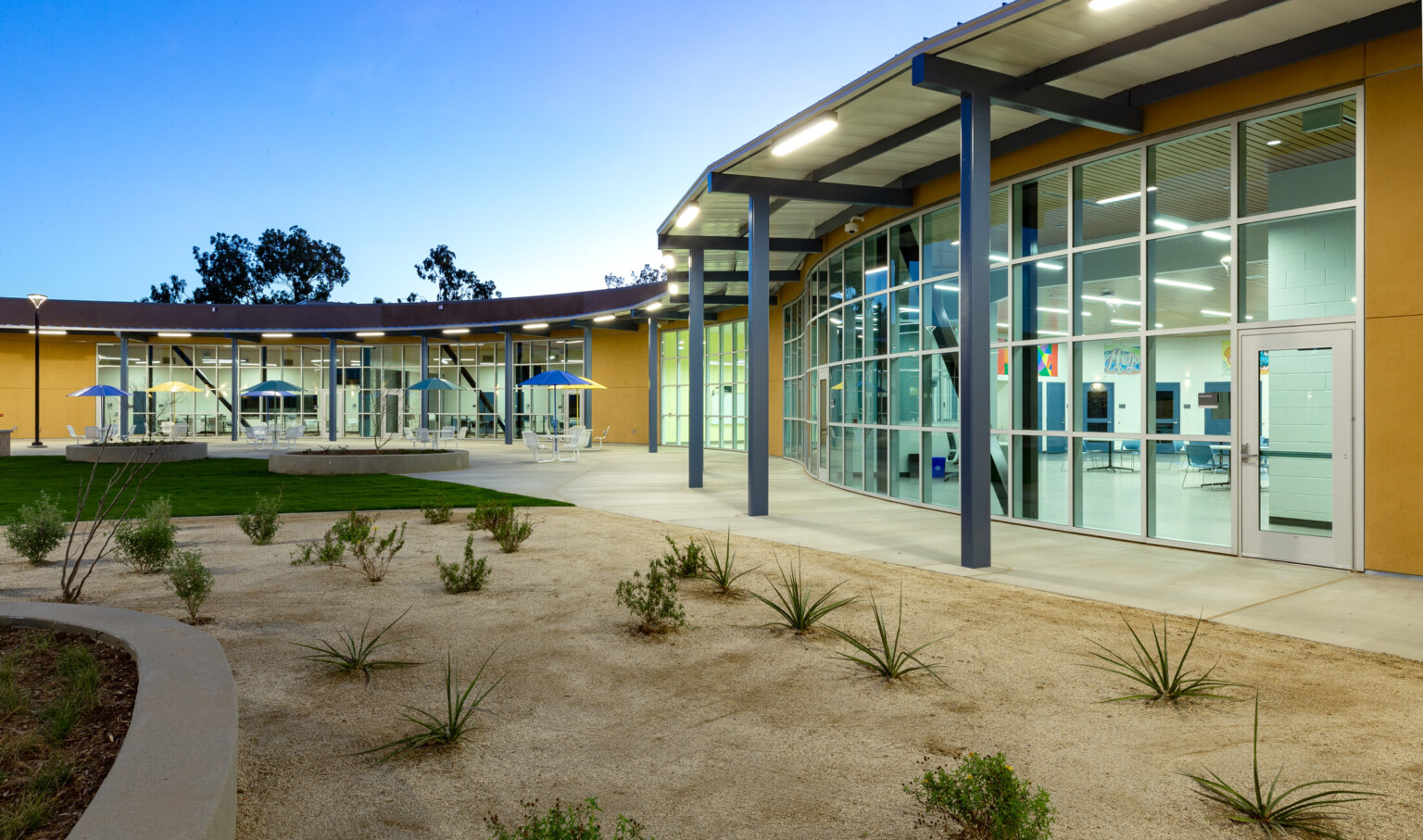 curved single story building with flat roof floor to ceiling glass facade with yellow panels. concrete paths in desertscape