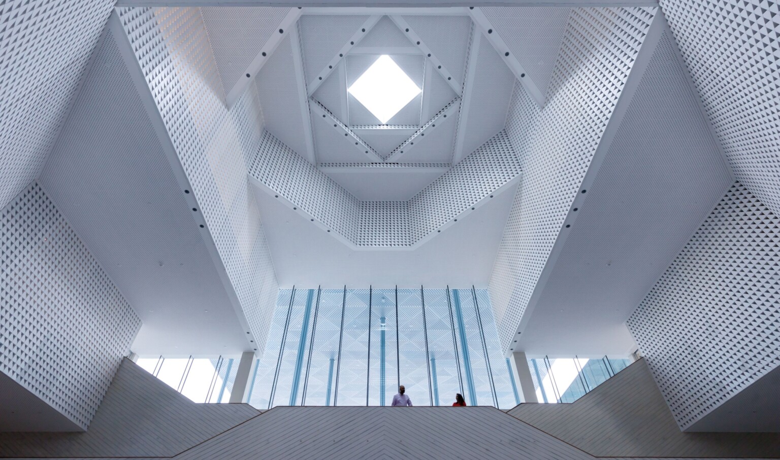 looking up at a detailed ceiling design at a community center; a skylight is the focal point with right angled wall jut-outs refracting the light throughout the space; eivan, iwan space