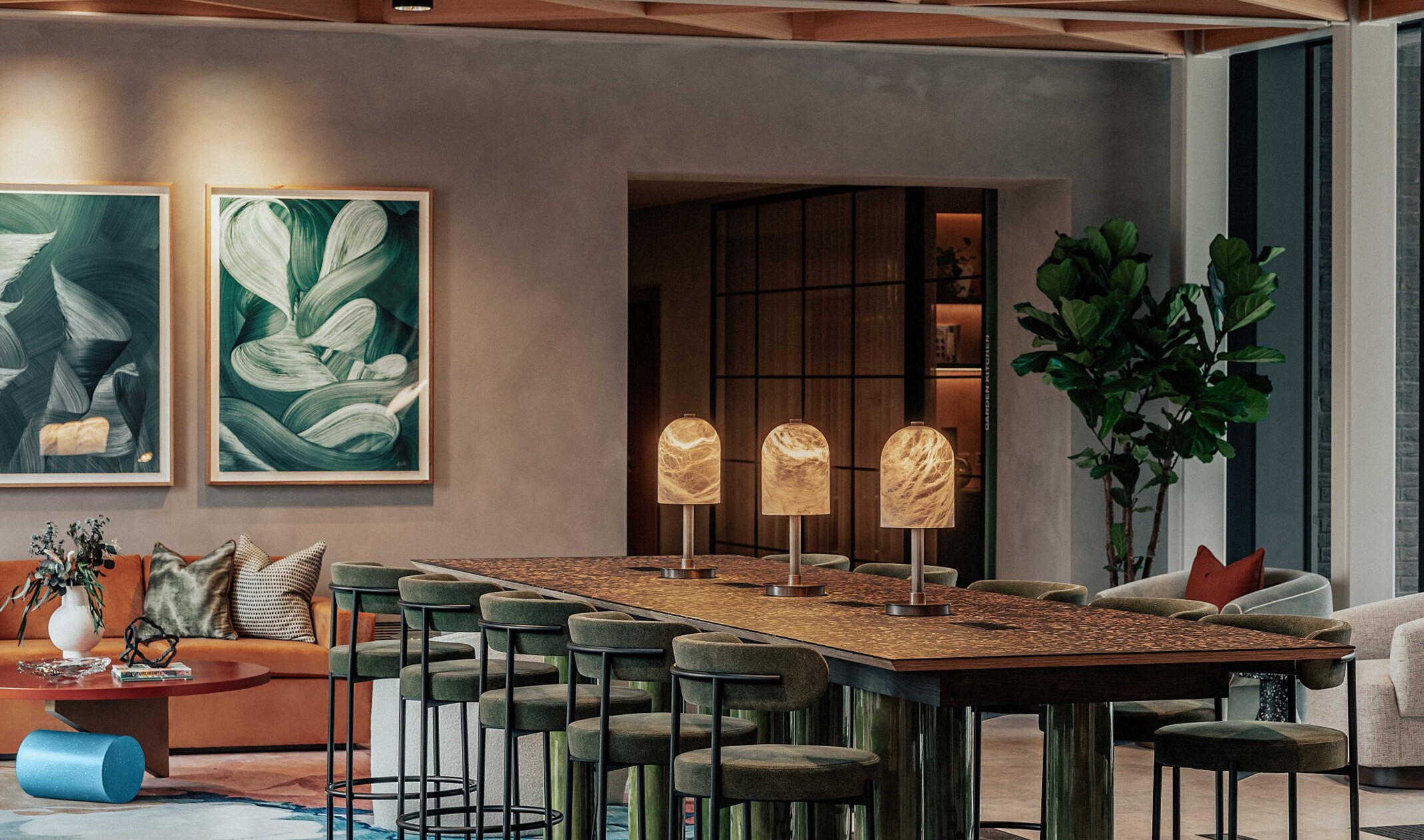 modern residential community space with a large table surrounded by green velvet seats; background art and sofa seating