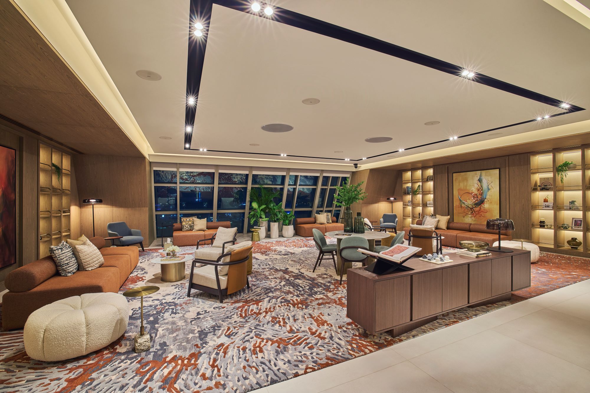 Modern office space filled with multiple seating areas, wooden furnishings, and a wall of windows to the back of the room