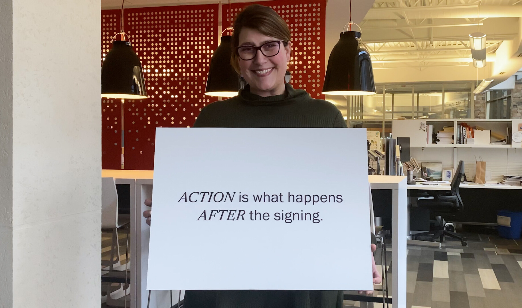 smiling woman in black holding a sign that reads action is what happens after signing