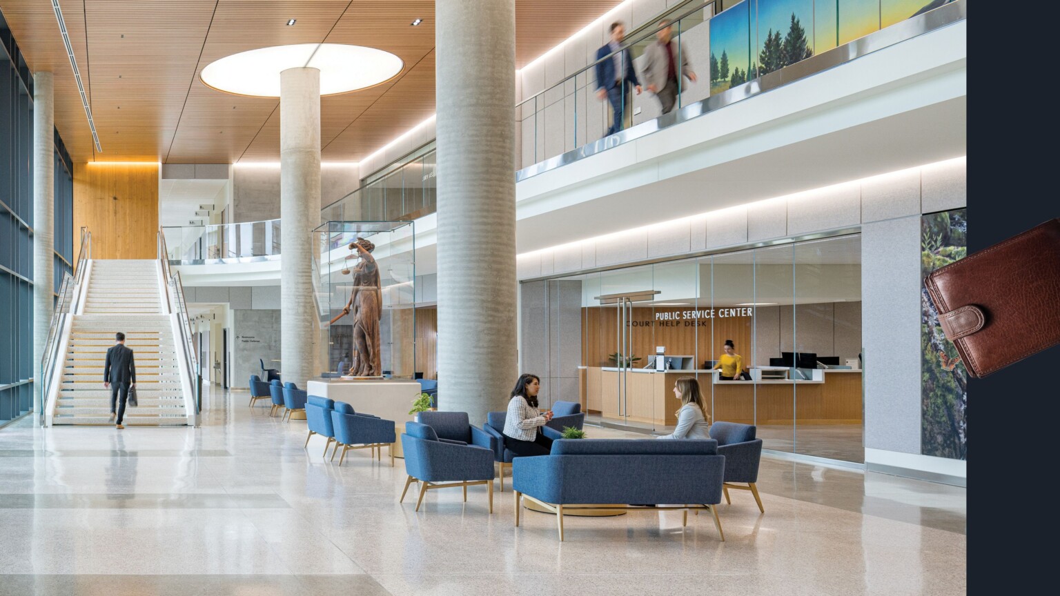 Grand entryway for the Clackamas County Courthouse showing a large stairway, column with a round opening to allow outside light into the building. The second story overlooks the first floor with glass railings; wallet graphic on the right side of image