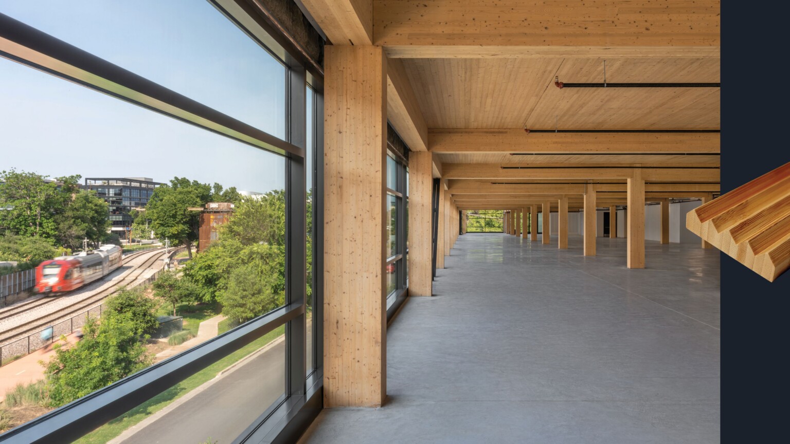 empty office building floor facing floor to ceiling windows; mass timber core building structure exposed; grooved wood emblem on the right of the image