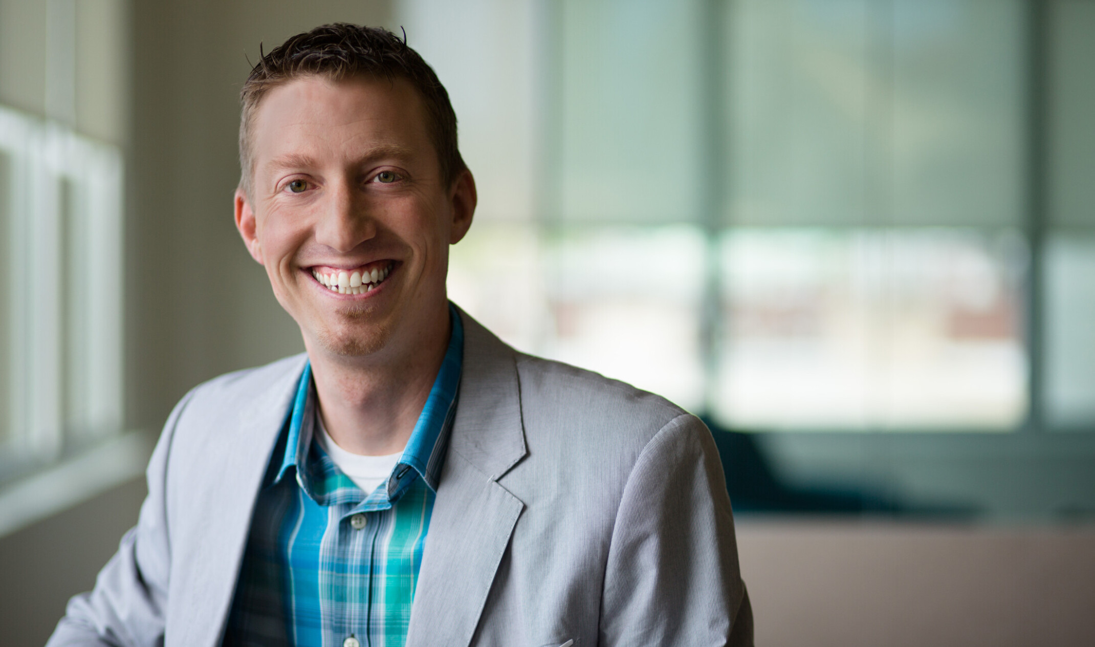smiling man in a beige suit jacket and blue plaid shirt