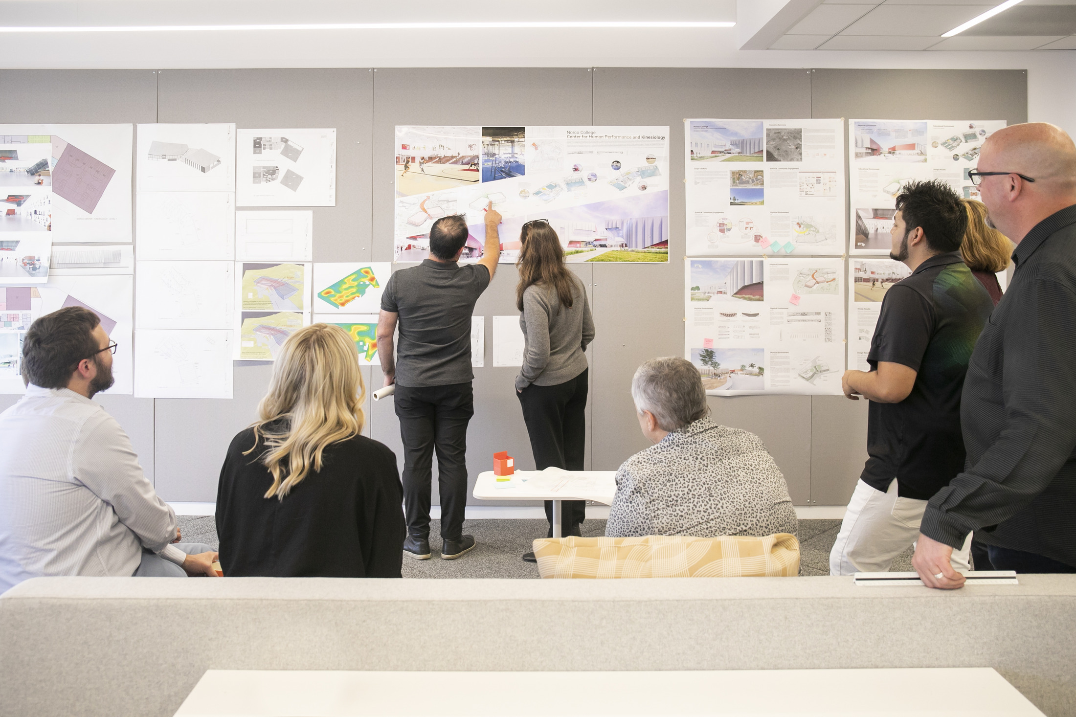 design leaders going through drawings together; sketches and architectural plans pinned up on wall