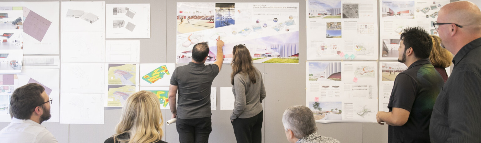 design leaders going through drawings together; sketches and architectural plans pinned up on wall