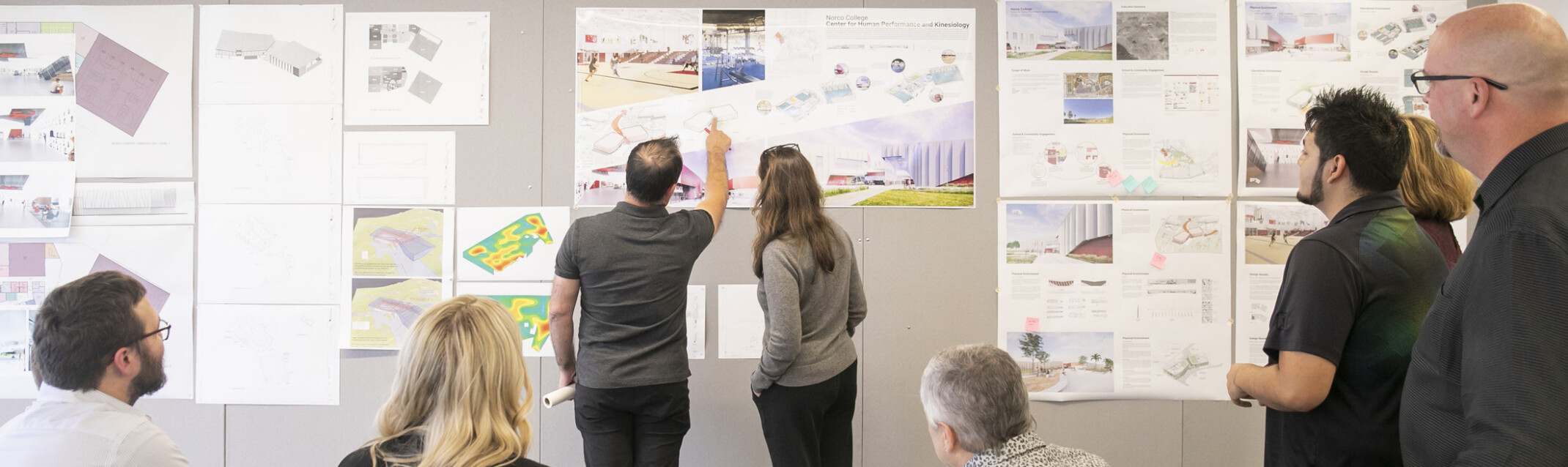 design leaders going through drawings together; sketches and architectural plans pinned up on wall