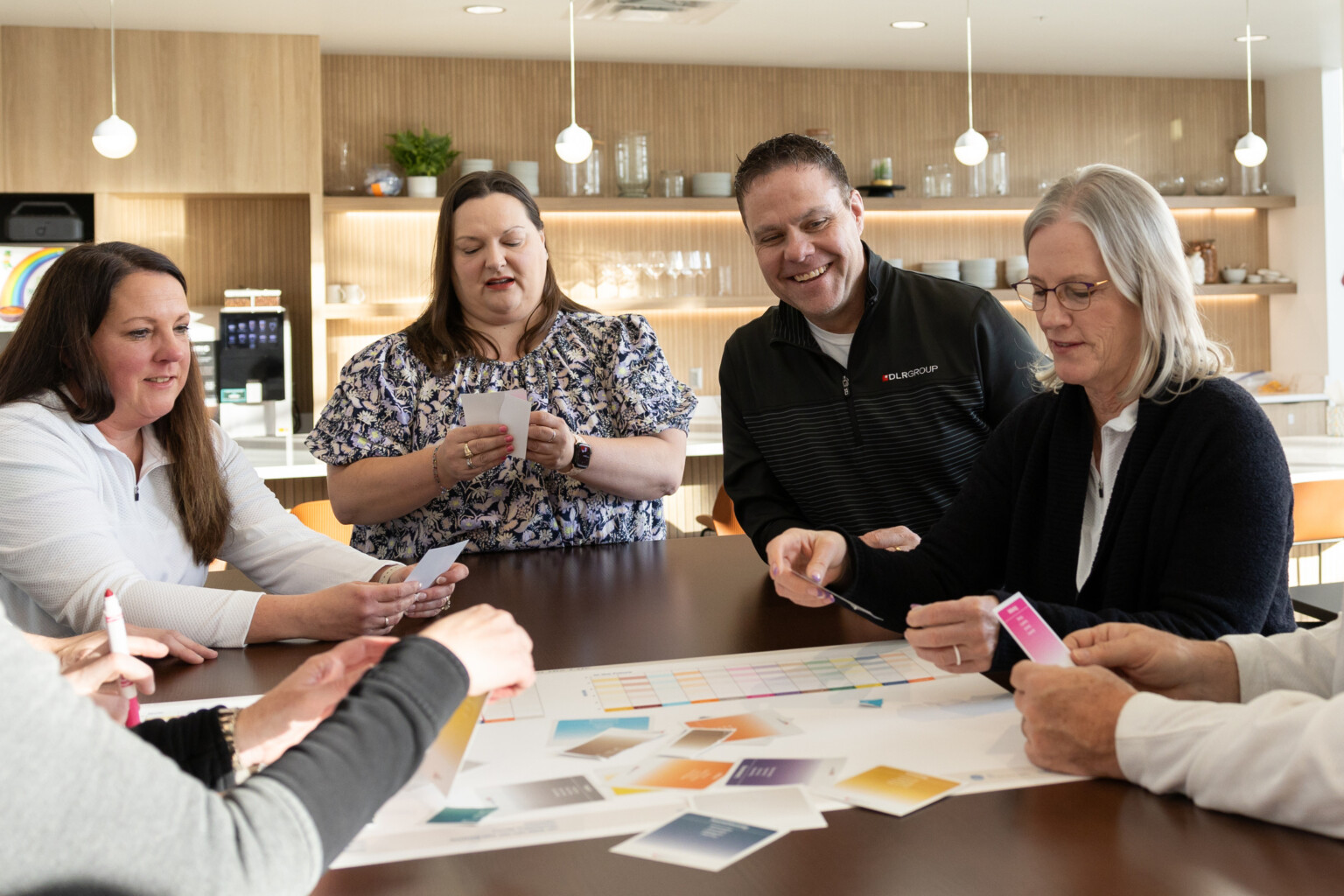a group of adults huddled around a corporate office kitchen collaborating with paper cards and a full page spread