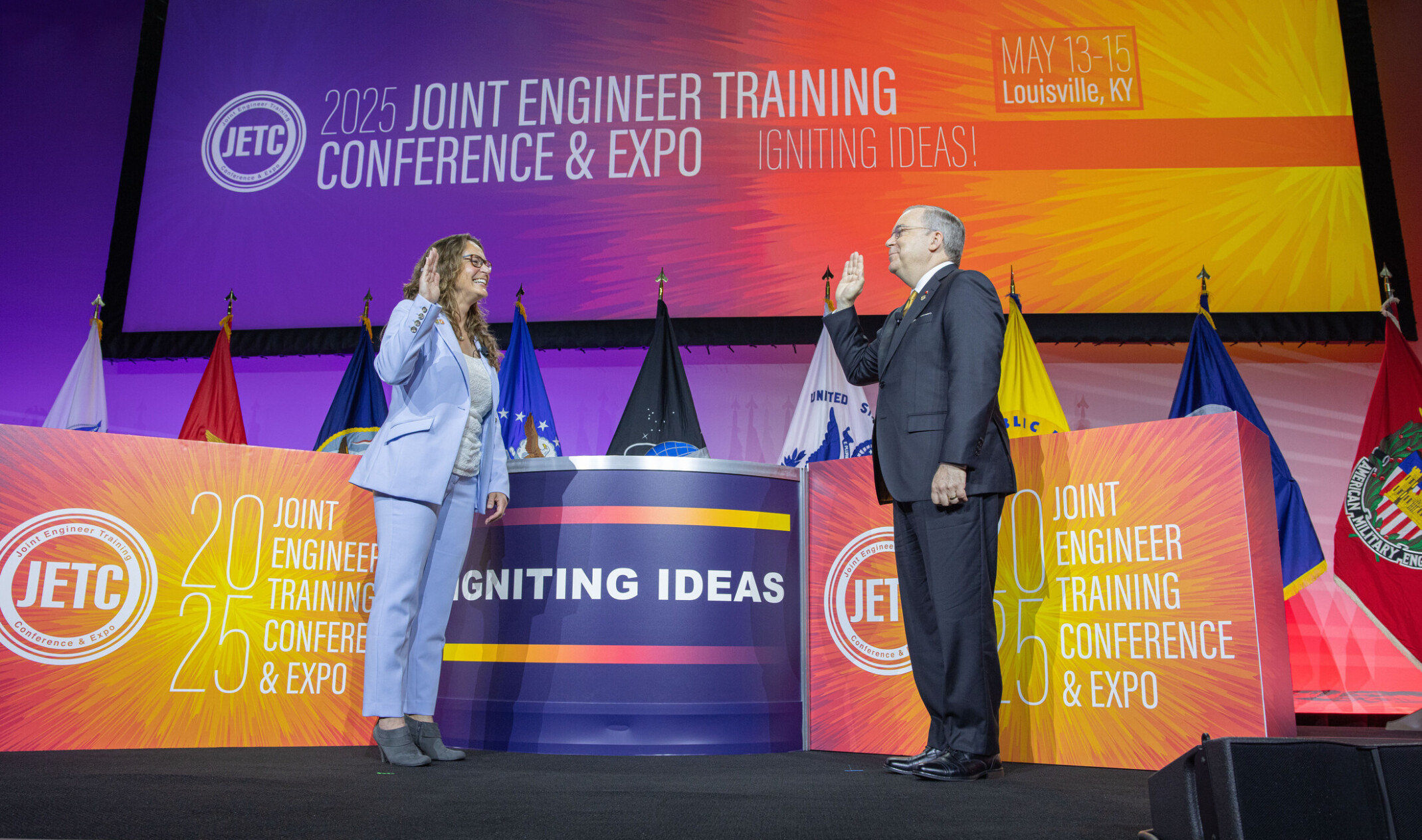 Michael Huffstetler sworn into the presidency of the Society of American Military Engineers; two people on facing eachother, right hands up with military flags and colorful banners behind them