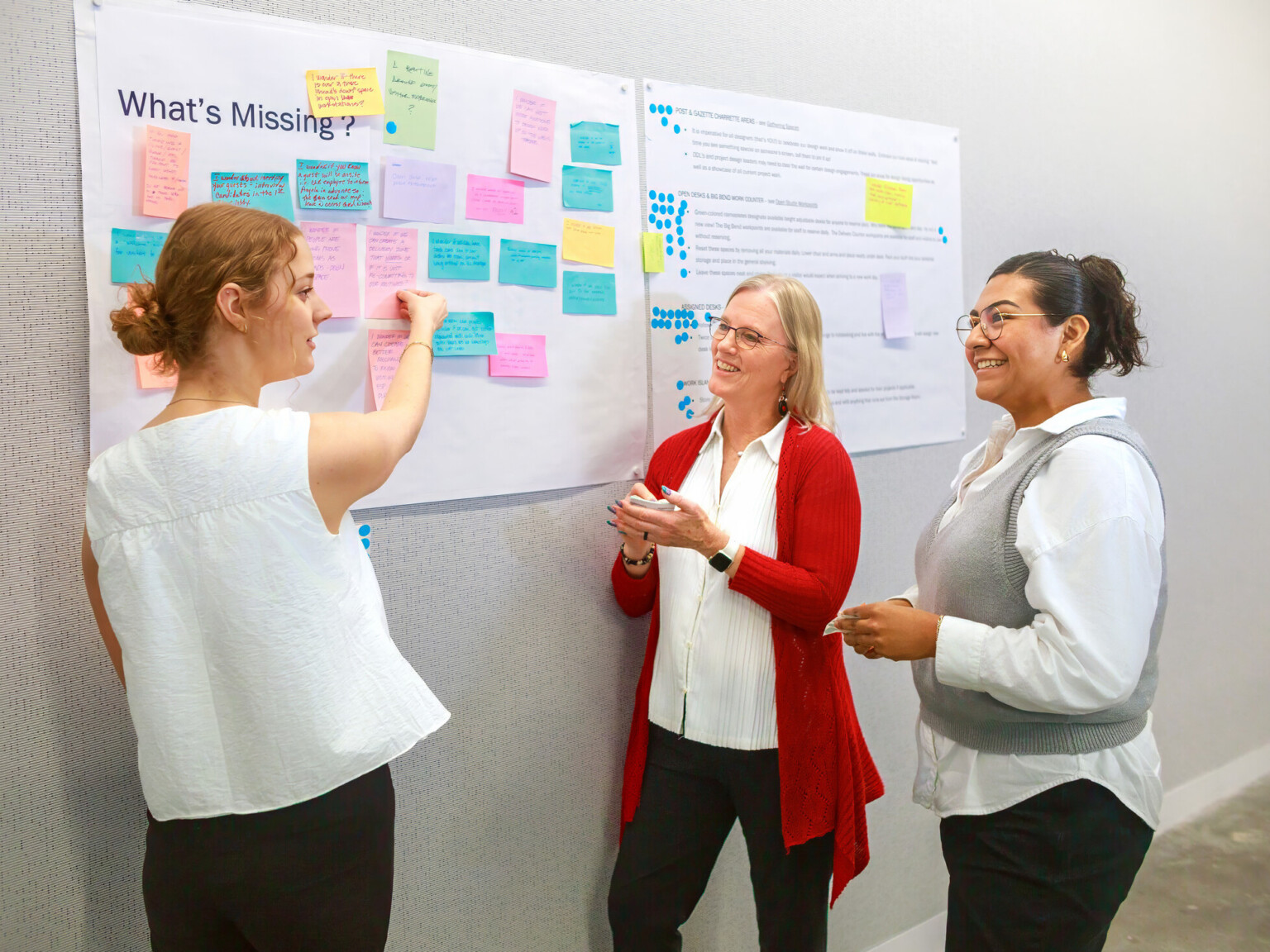 three women at a whiteboard collaborating with sticky notes and paper