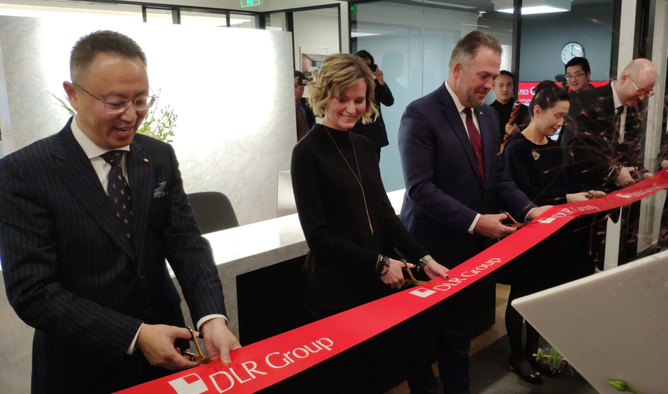 Shanghai, China DLR Group Office Expansion ribbon cutting. Red ribbon with company logo hangs, with 5 people cutting it