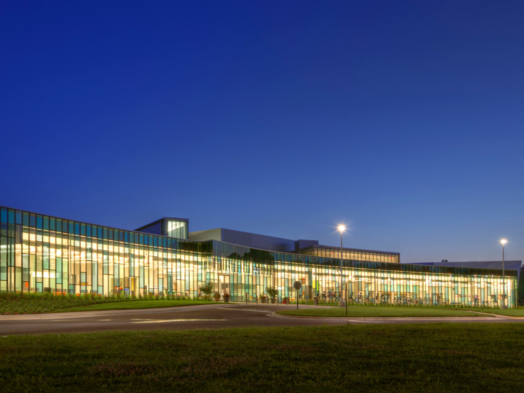 nighttime image of a building with colorful floor to ceiling windows with grass and walkways in the foreground