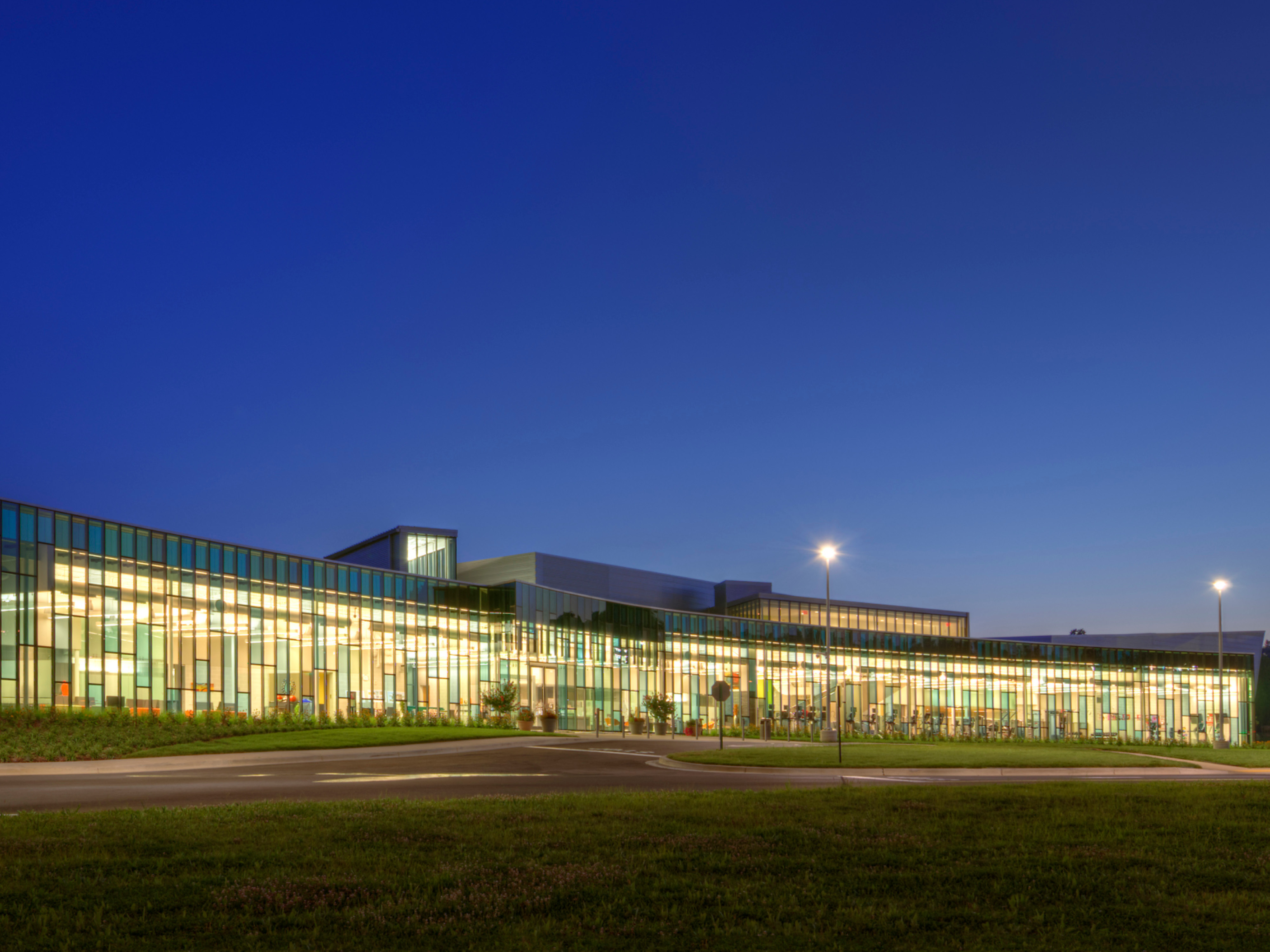 nighttime image of a building with colorful floor to ceiling windows with grass and walkways in the foreground