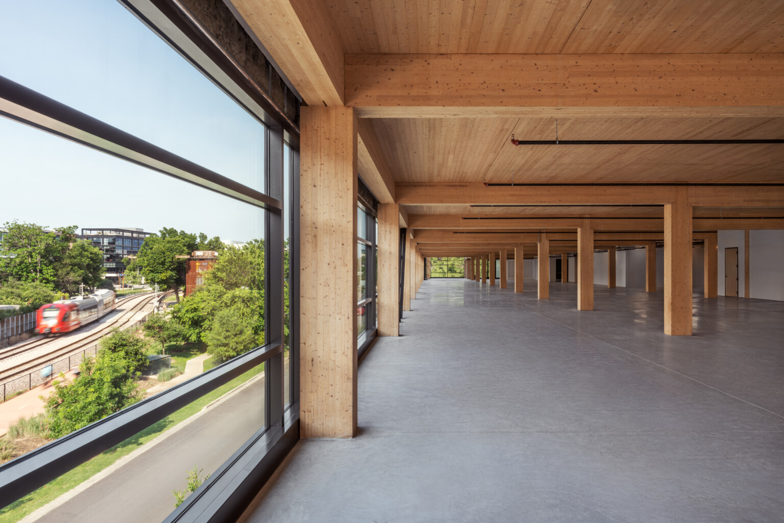 Mass timber open floor plan office space with exposed wood cieling and beams, raw concrete floor, floor to ceiling windows Mass timber open floor plan office space with exposed wood cieling and beams, raw concrete floor, floor to ceiling windows