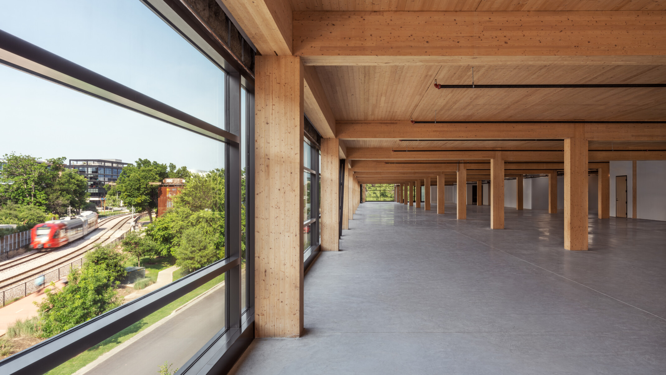Mass timber open floor plan office space with exposed wood cieling and beams, raw concrete floor, floor to ceiling windows