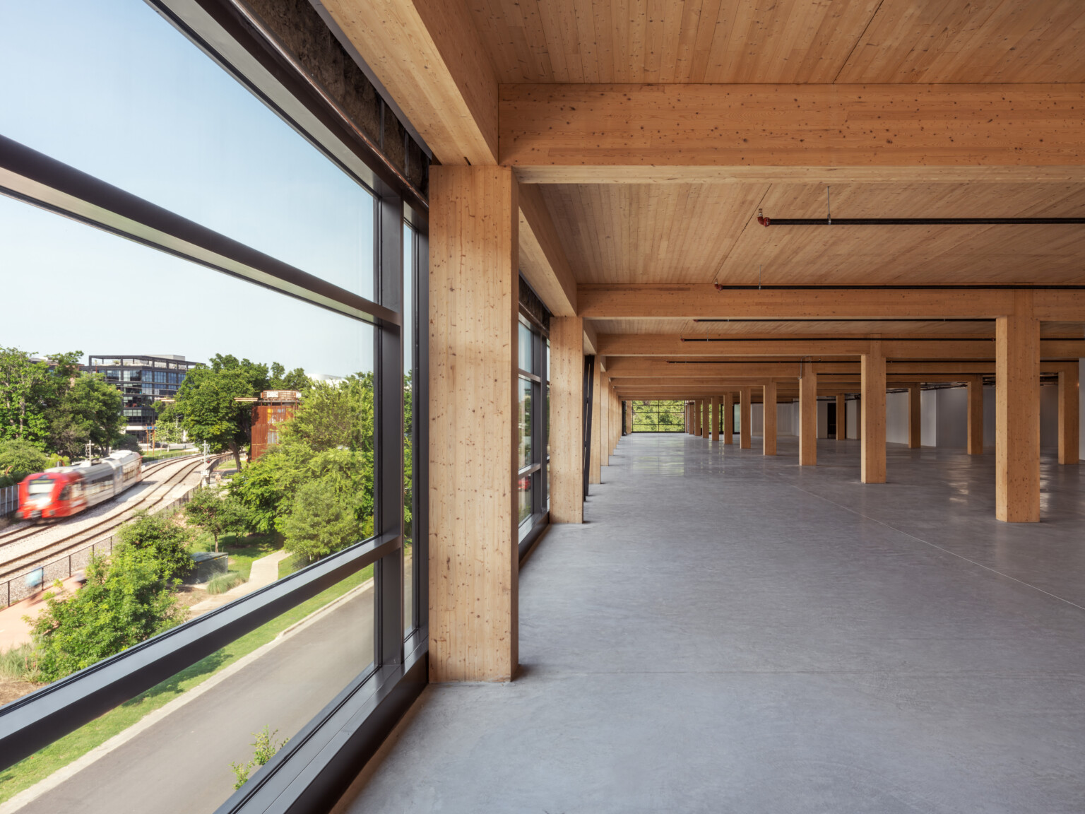 Mass timber open floor plan office space with exposed wood cieling and beams, raw concrete floor, floor to ceiling windows