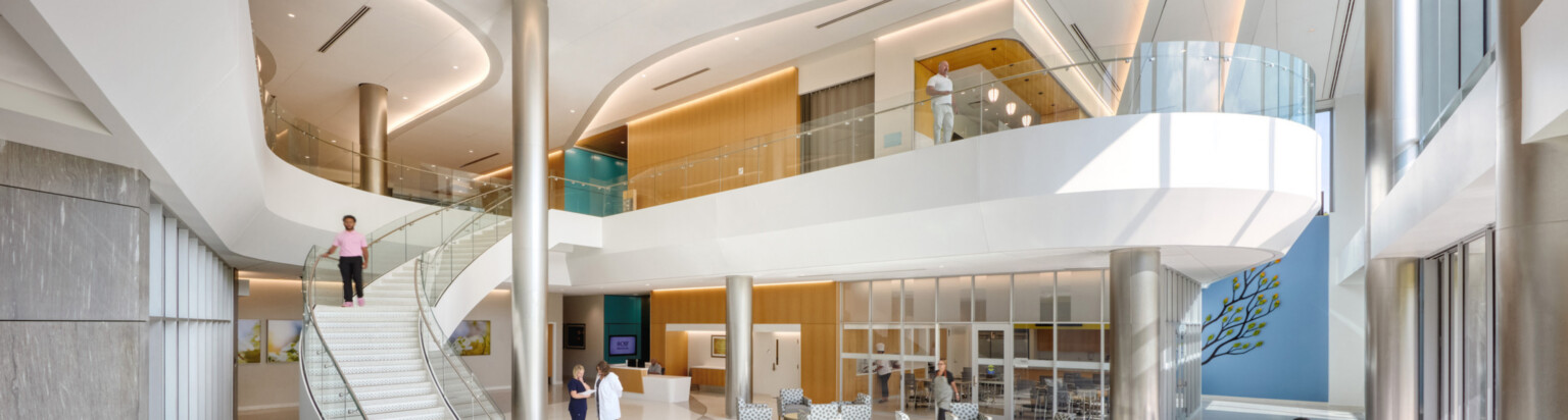 Inside image of OSF Cancer Institute and Proton Therapy; Modern, sleek and mostly white design with balcony and staircase down to the waiting area