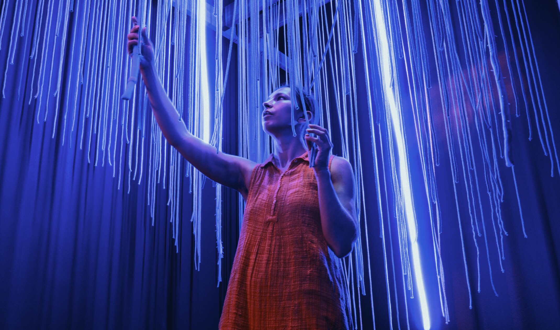 woman standing in a blue lighted room with tactile and sensory elements around her; camera shot from the ground up point of view. Photo by Hamilton Jones