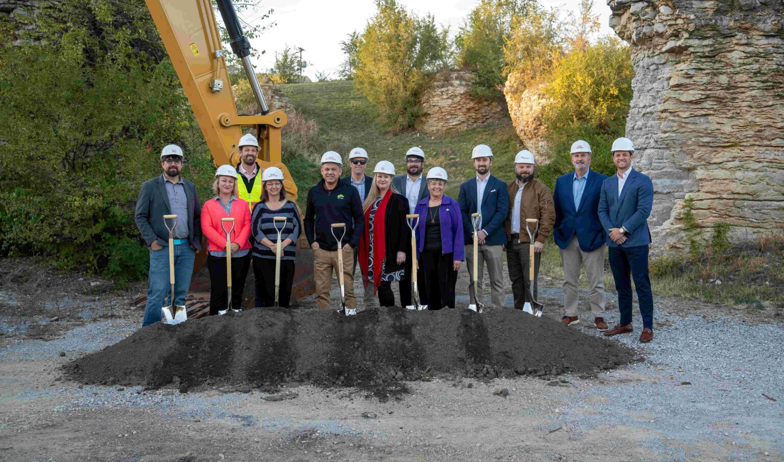 The Rocks mixed-use development groundbreaking ceremony; 14 people in construction hats standing in front of a pile of dirt with shovels