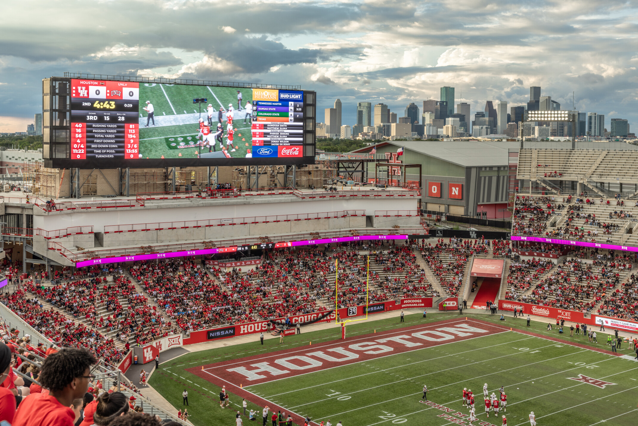 Football stadium filled with fans showing a large scoreboard with a view of skyscrapers in the background.