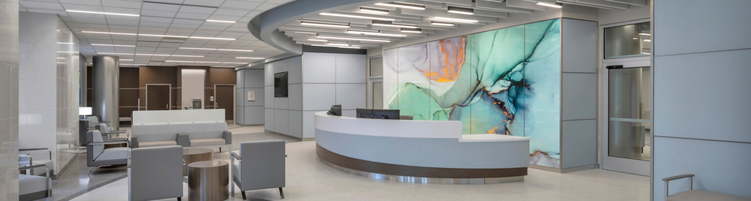 Hospital waiting room with grey and white floors, dark brown accent wall, with a modern geode mural on the wall behind a desk.