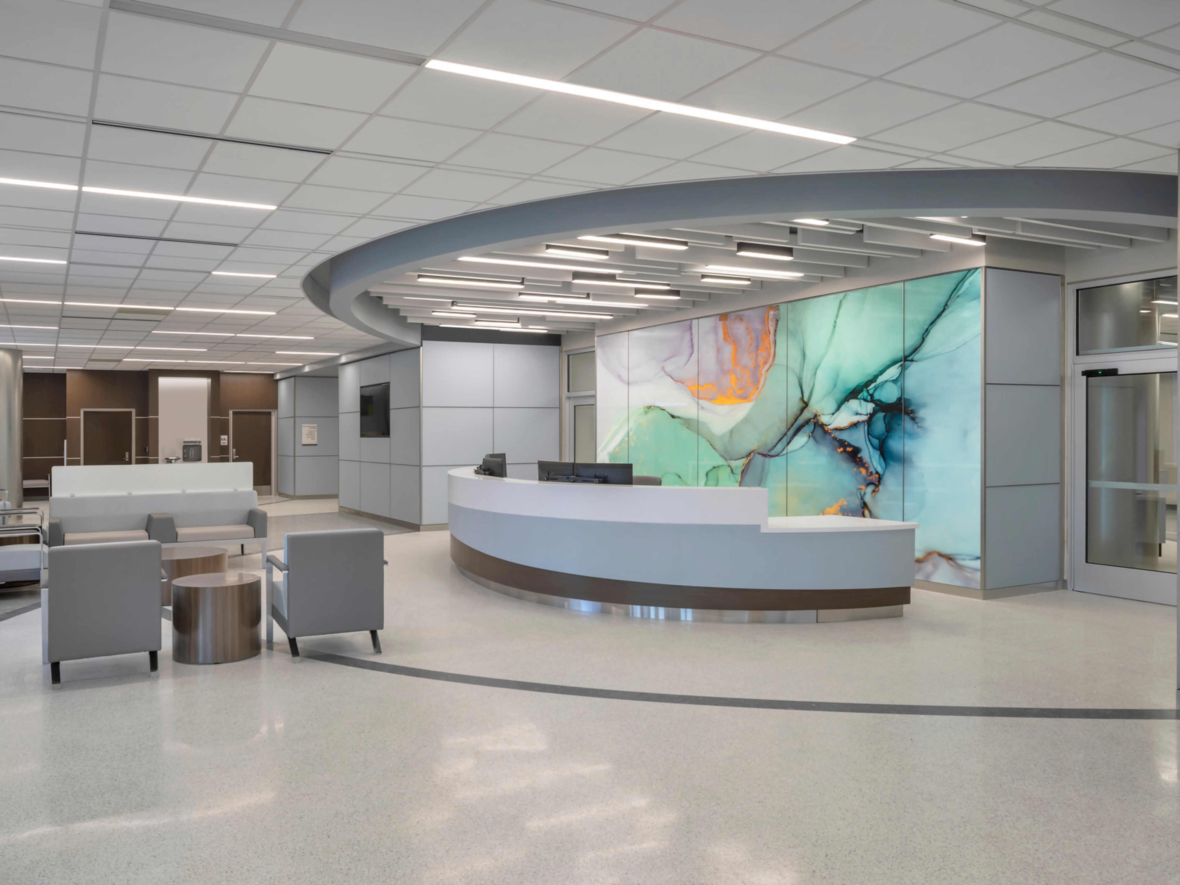 Hospital waiting room with grey and white floors, dark brown accent wall, with a modern geode mural on the wall behind a desk.