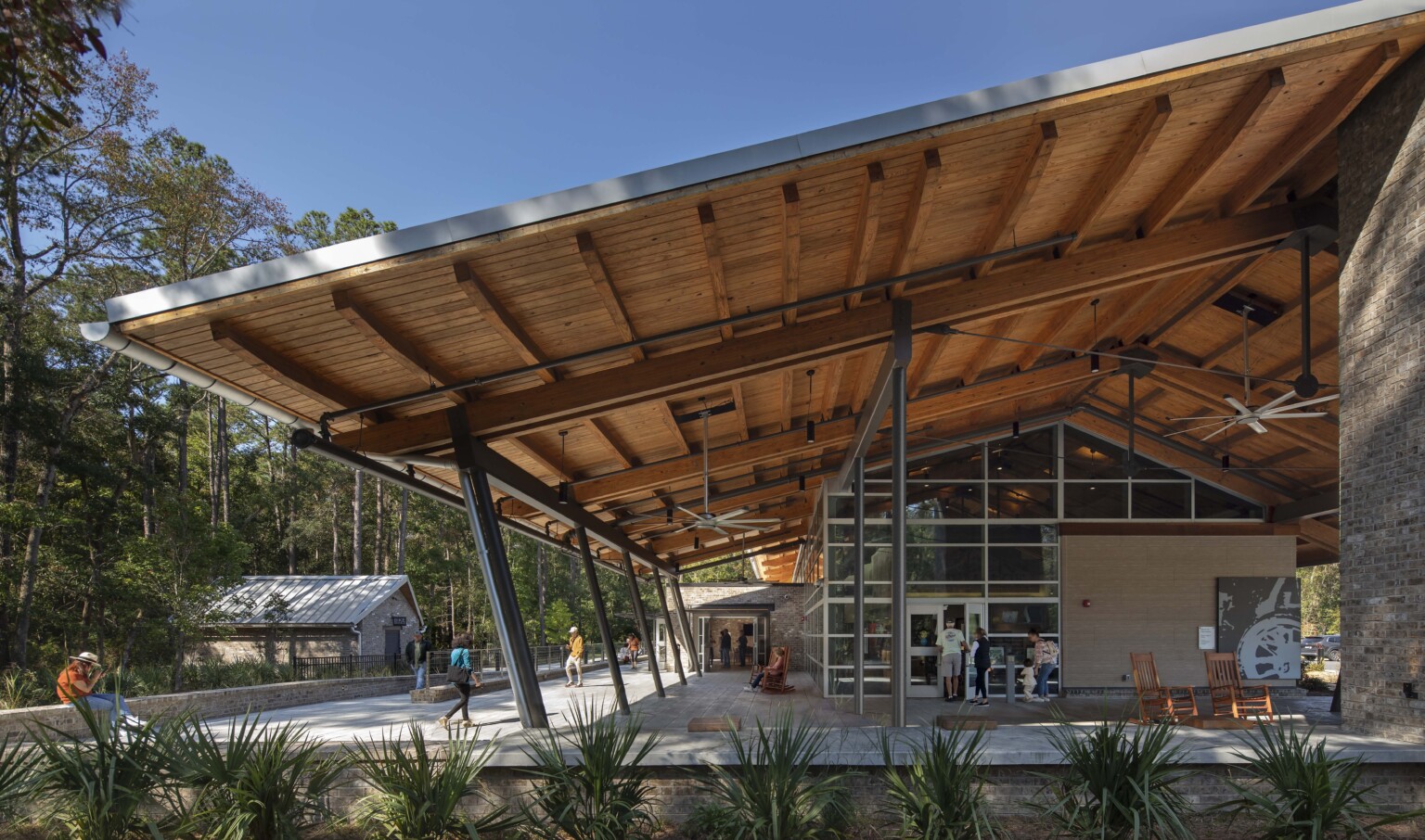 Wormsloe State Park visitor center; mass timber structure awning with glass walls for natural light; people outside the building sitting and walking in surrounding nature