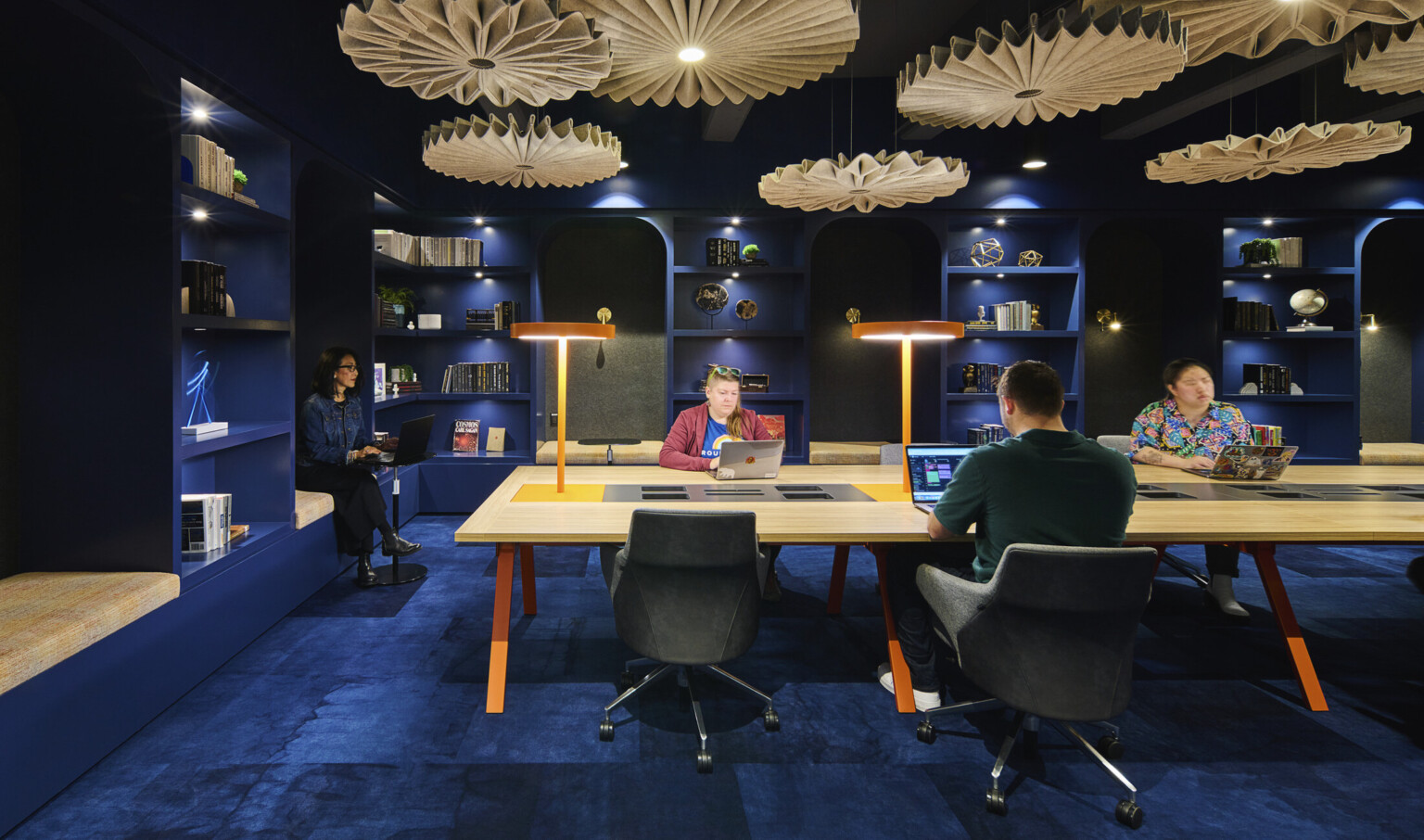 Blue room office common space with long table with built in lights. Sculptural organically shaped illuminated beige accents hang