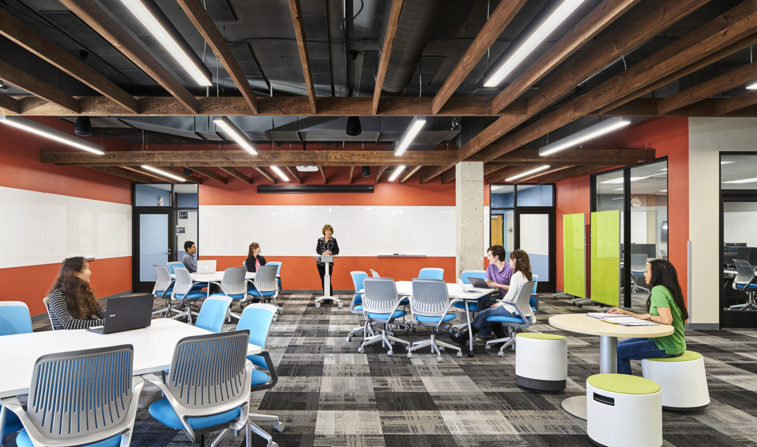 students learning in a room with flexible furniture and timber ceilings. Orange and white striped wall, front and left