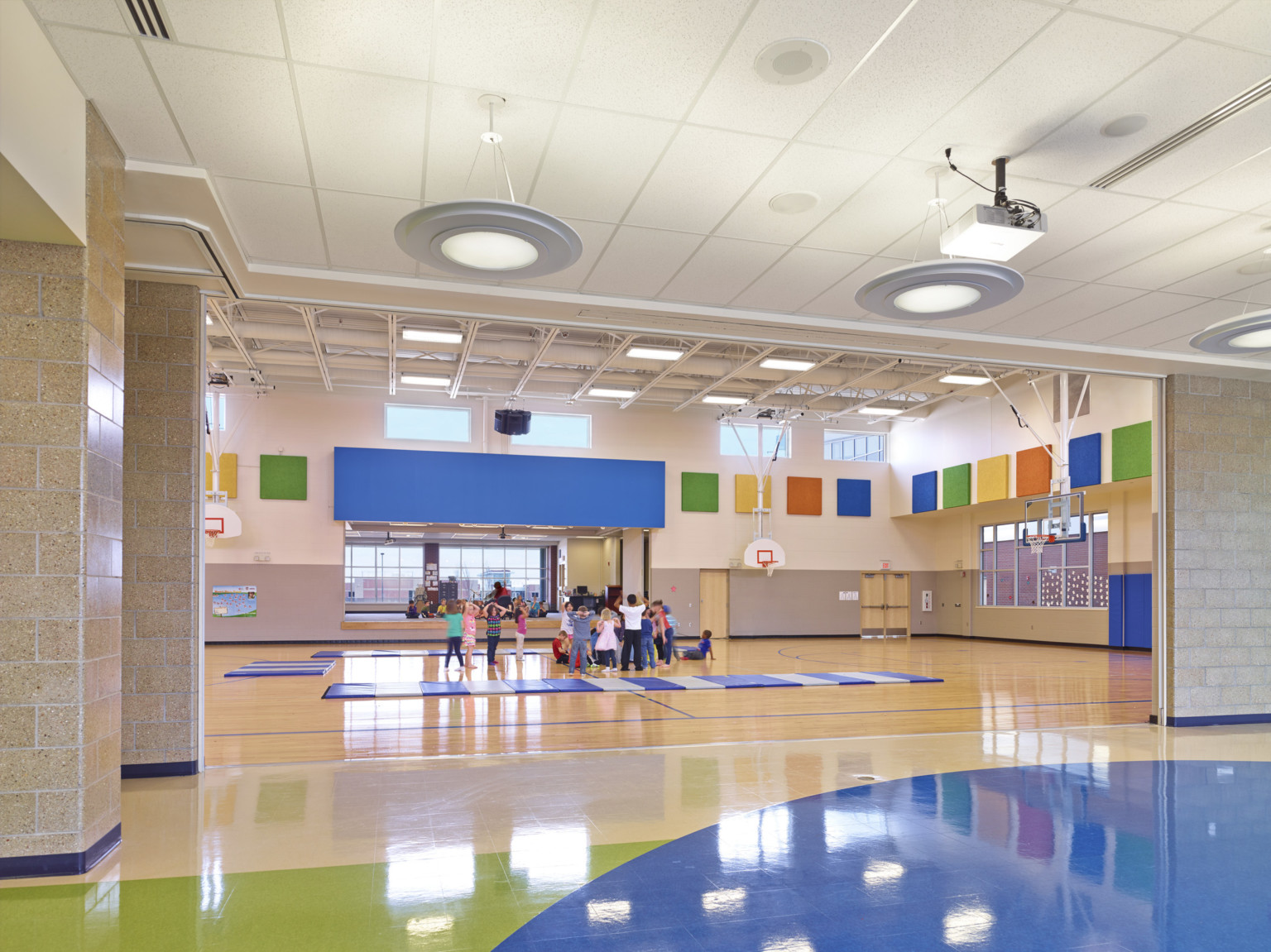 gymnasium at middle school with colorful panels along upper wall and blue padded mats laid on the ground around the children