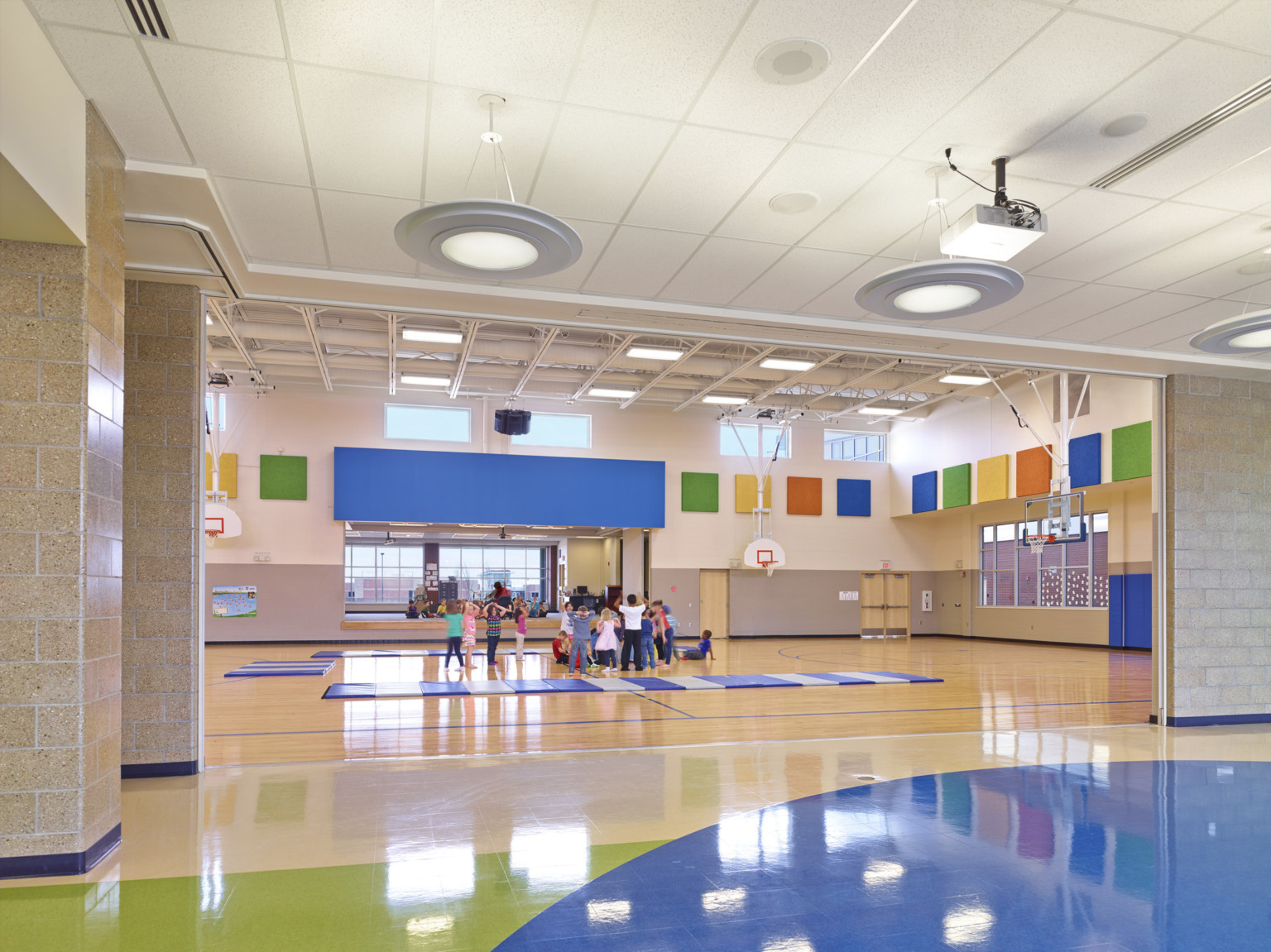 gymnasium at middle school with colorful panels along upper wall and blue padded mats laid on the ground around the children gymnasium at middle school with colorful panels along upper wall and blue padded mats laid on the ground around the children