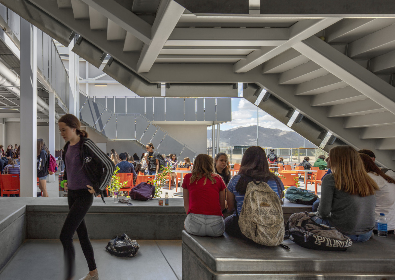 view of students in a covered, multiple story outdoor seating area beneath communicating stairs at canyon view high school