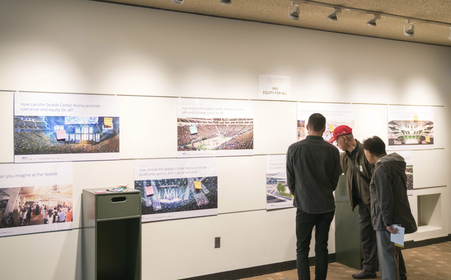 Three men pointing at a photo on white gallery wall in Seattle Three men pointing at a photo on white gallery wall in Seattle