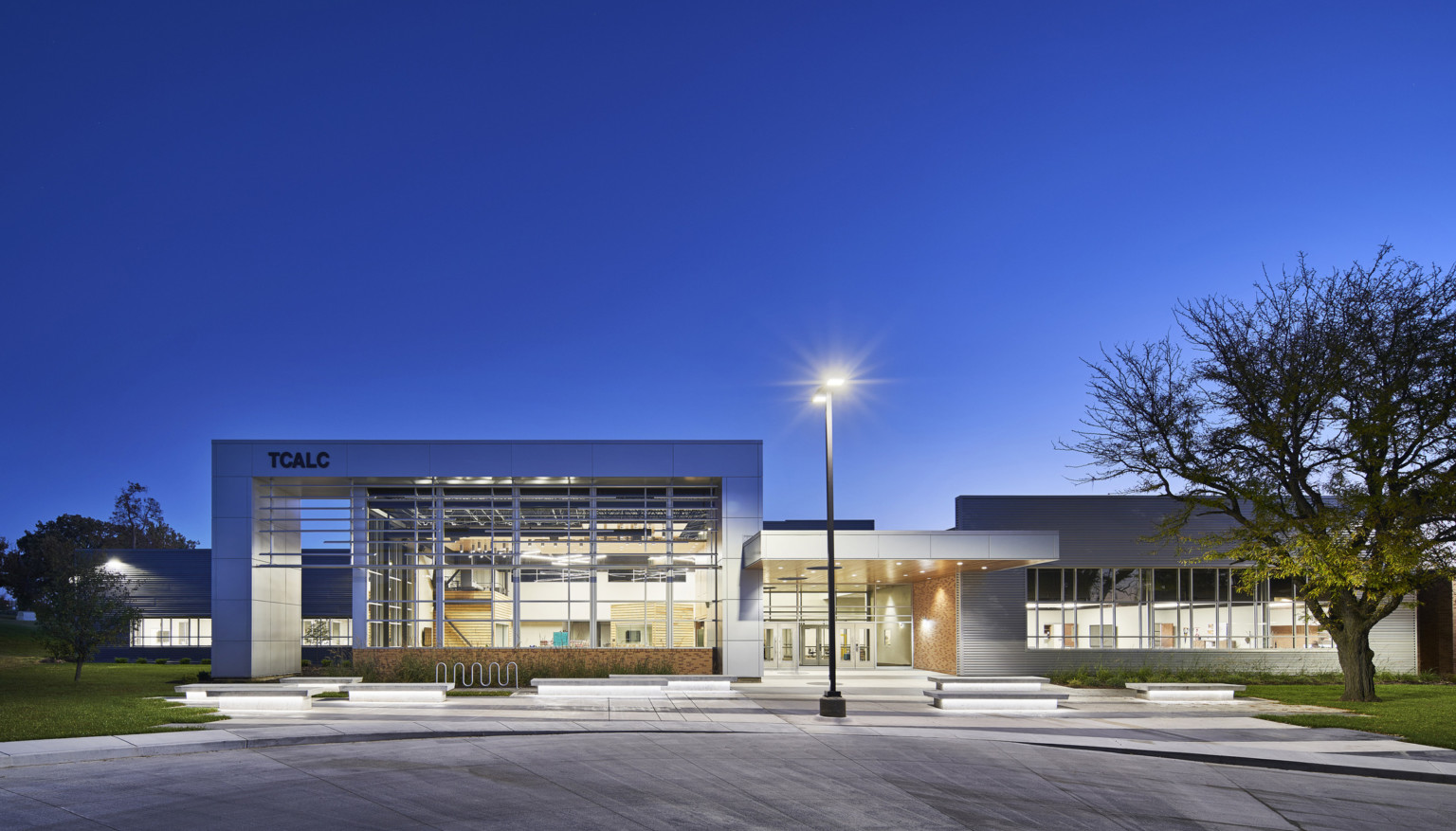 evening exterior view of school with floor to ceiling windows and lighting at Topeka Center for Advanced Learning & Careers evening exterior view of school with floor to ceiling windows and lighting at Topeka Center for Advanced Learning & Careers