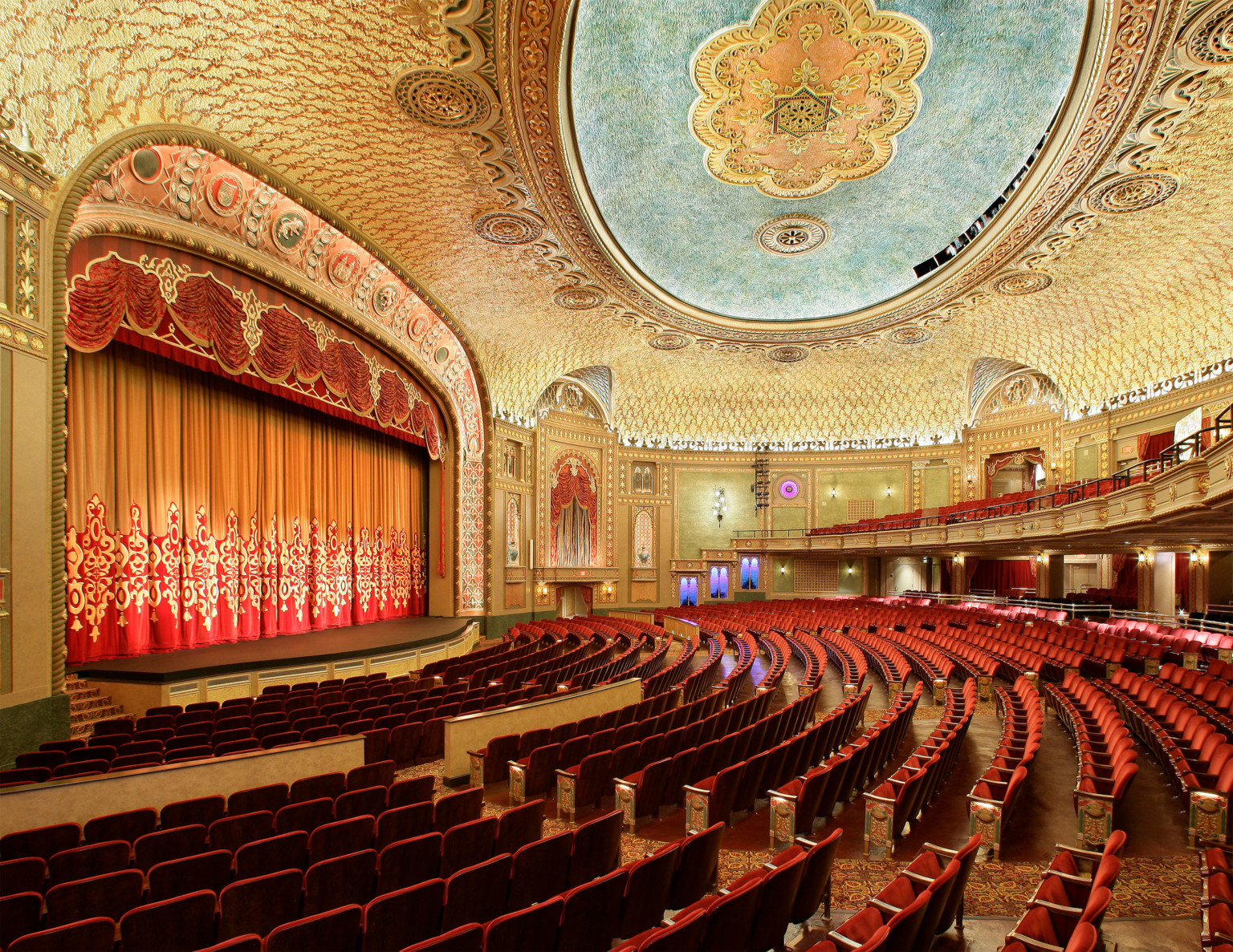 Historic grand theater with red seating, grand ornate archway over stage, red drop curtain, and gold ceiling at the Tennessee Theater