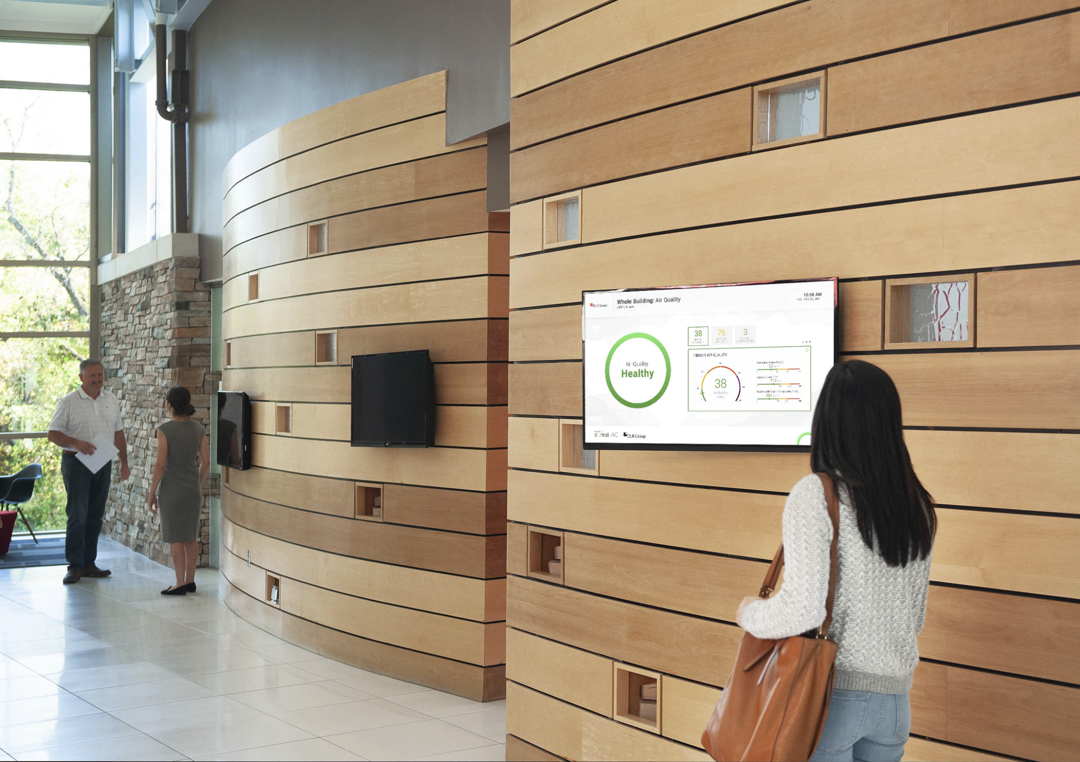 woman walking past interactive screen showing air quality in the workplace with wood panel wall and large window opposite
