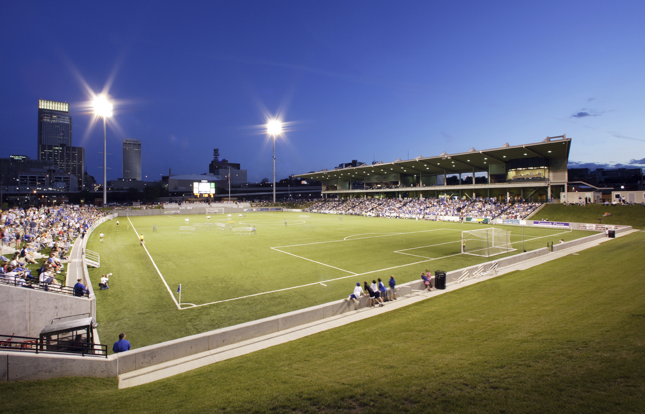Morrison Stadium at Creighton University soccer field from grass lawn of stadium with sideline seating, illuminated at night