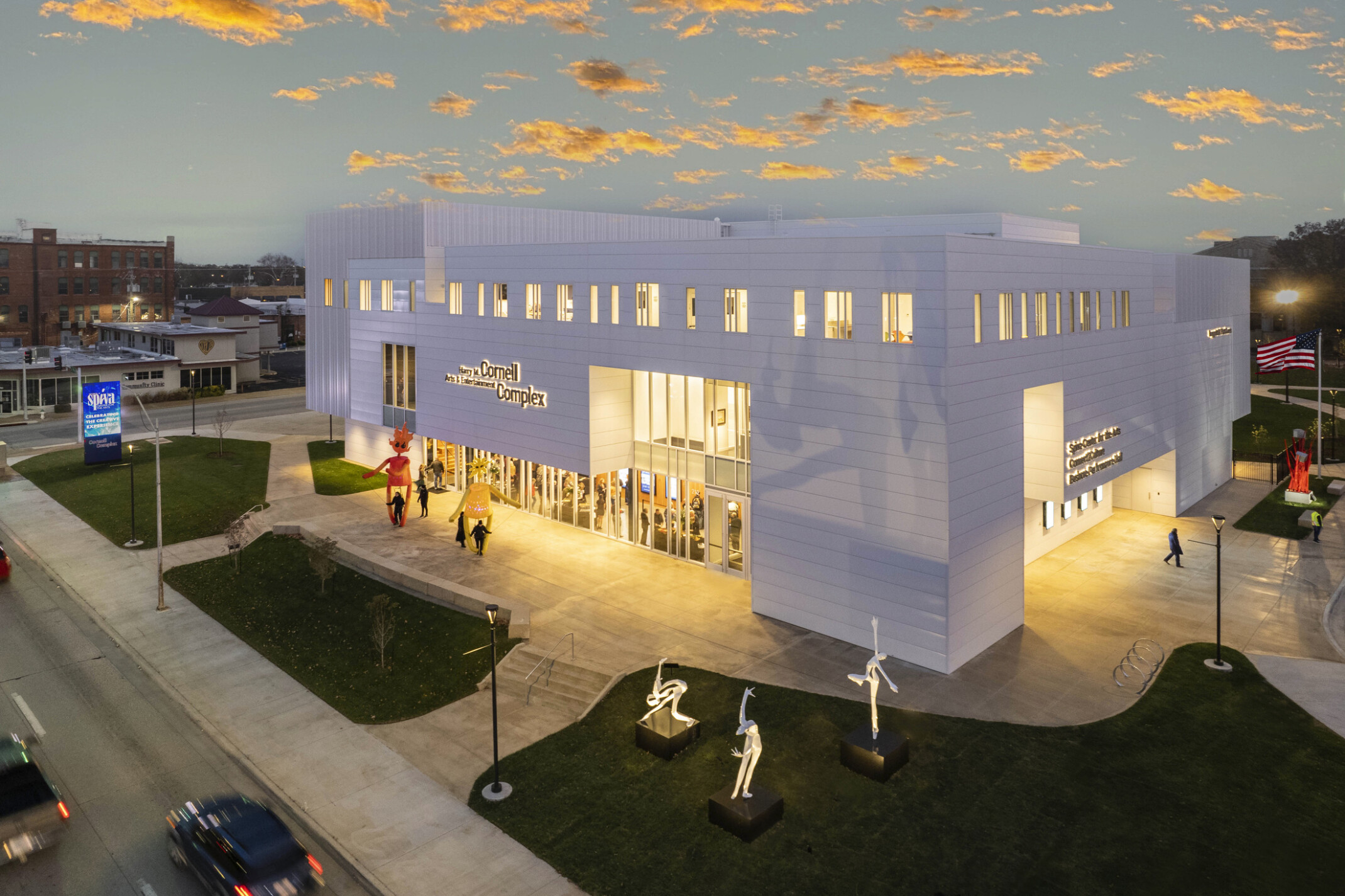 Exterior, night-time view of the new Harry M. Cornell Arts & Entertainment Complex, a white paneled building, sculptures on lawn