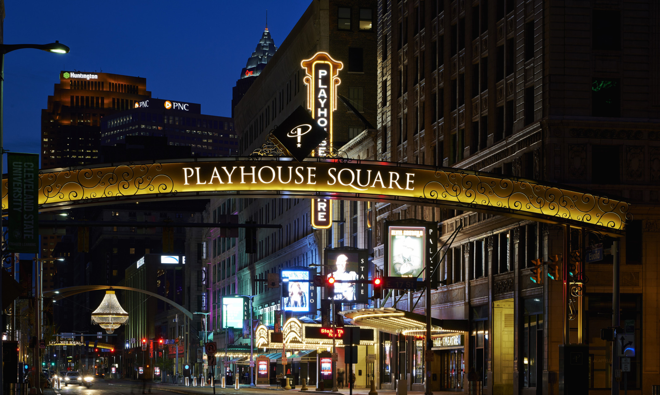 Sign reading Playhouse Square illuminated at night with scroll detailing on both sides in front of block of tall buildings