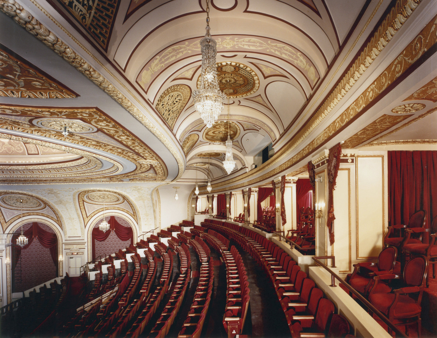 Box seats and back rows of audience in the Connor Palace Theater, with red seats and white walls with gold scroll details