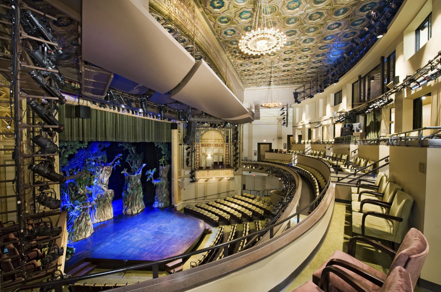 Multiple balconies in a theater with yellow seats and dark details, box seat center with arch overhang and gold details