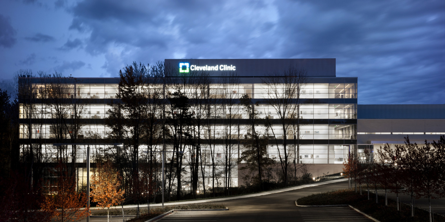 Exterior view of building illuminated at night with bottom floor built into hill. Lit sign at top reads Cleveland Clinic