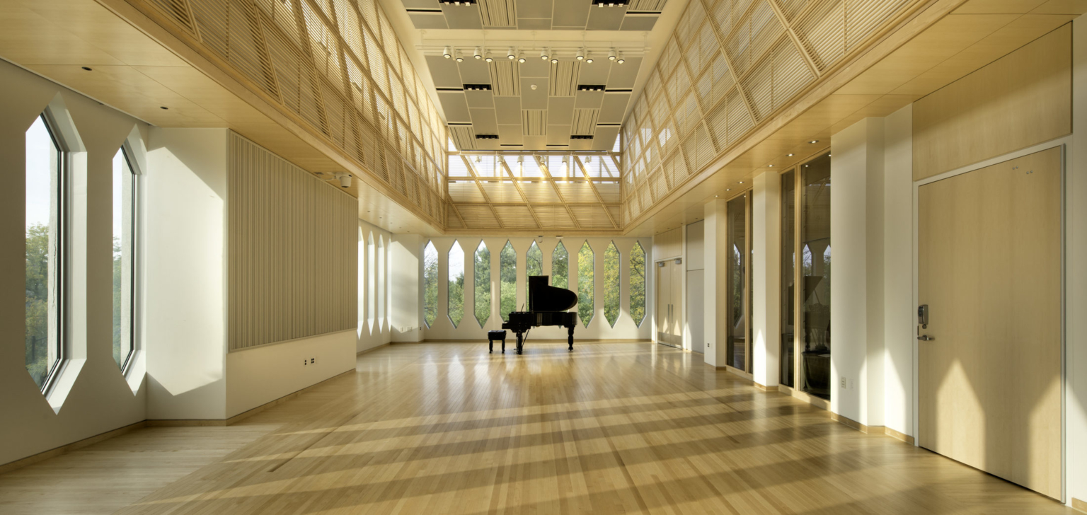 Piano in performance area with diamond shaped windows, warm wood paneling, and high ceilings