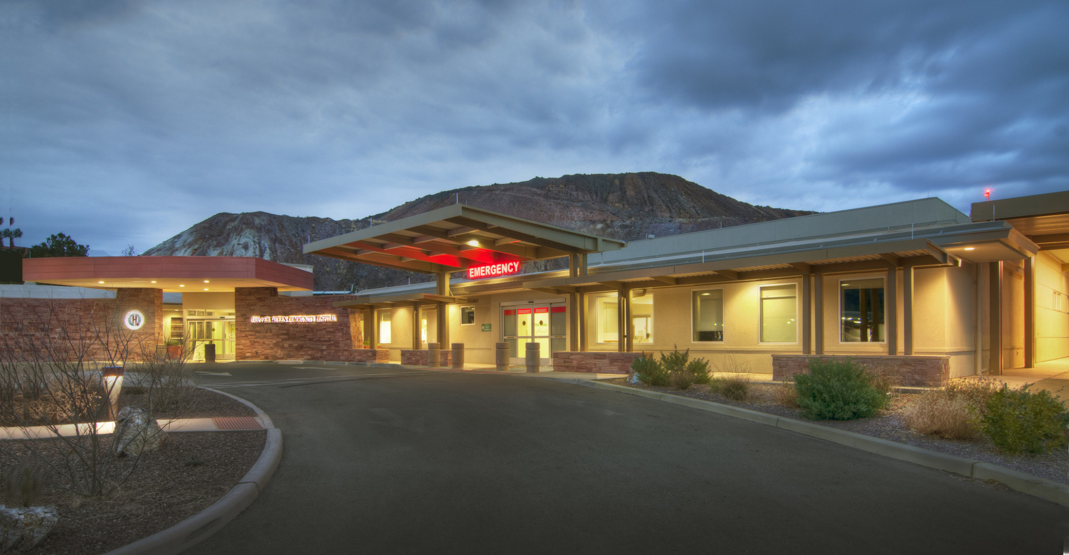 Exterior view of the Copper Queen Community Hospital Emergency Room entrance illuminated at night in front of mountain
