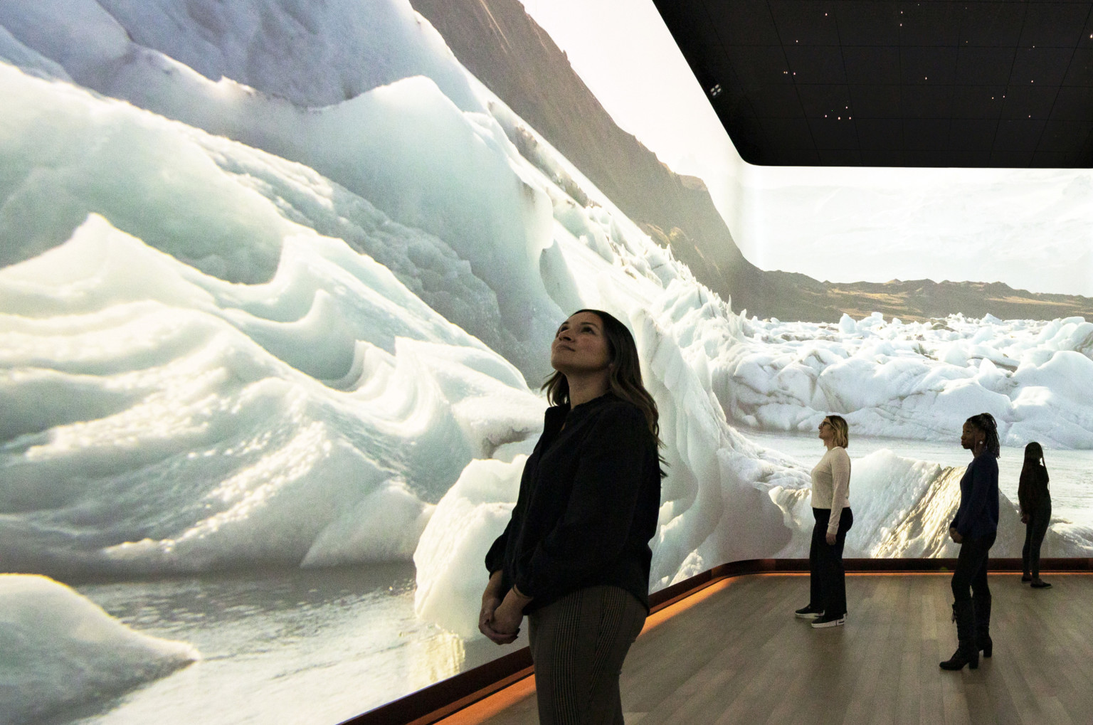 Woman stands in front of immersive 360 degree video art display of snow dunes and ice