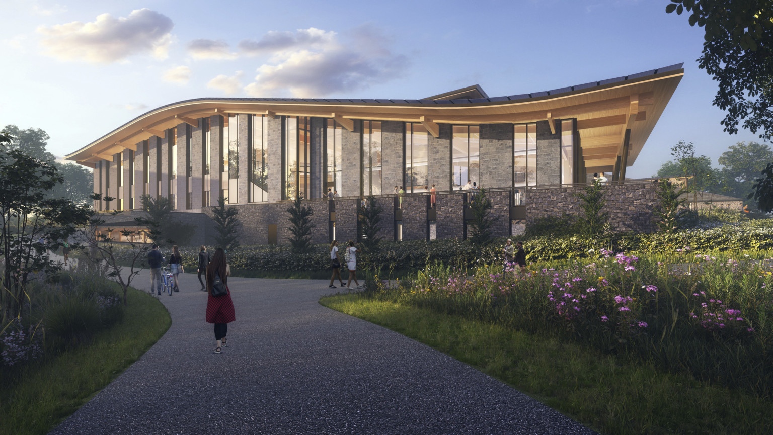 Walking path lined with flowers and greenery to stone and glass building with curving roof and overhang Walking path lined with flowers and greenery to stone and glass building with curving roof and overhang