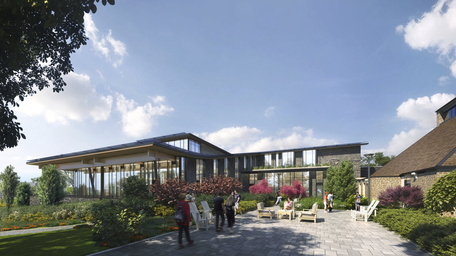 Exterior of stone courtyard in back of building with seating, surrounded by plants and greenery. Large windows face area Exterior of stone courtyard in back of building with seating, surrounded by plants and greenery. Large windows face area